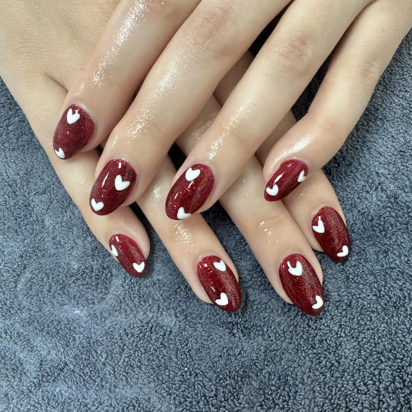 Burgundy nails with hand-painted white hearts, done at Just Spa & Nails
